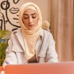 Focused young Muslim woman working on a laptop at a cafe.